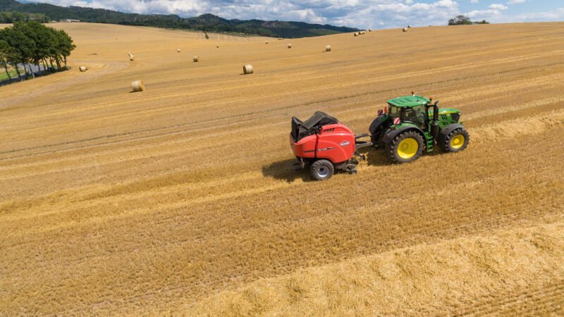 Vue d'ensemble d'une presse VB 7190 dans un champ de paille avec des balles rondes sous un beau ciel