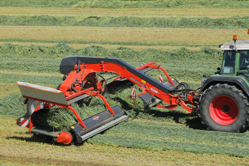 Photo de l'andaineur à tapis MERGE MAXX 950 au travail en dépose centrale dans une prairie