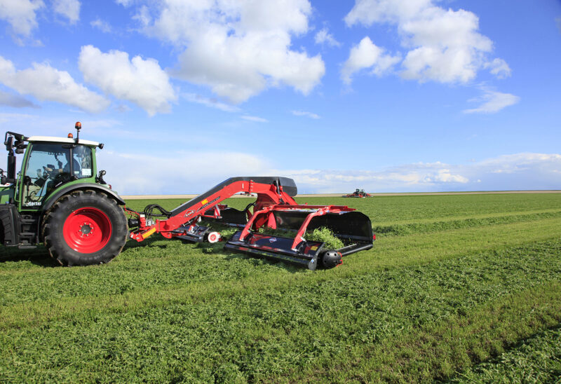 Photo de l'andaineur à tapis MERGE MAXX 950 au travail en dépose centrale dans une parcelle de luzerne